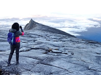 Solo woman traveler taking a picture of South Peak, top of mountain Kota Kinabalu, Sabah State,...