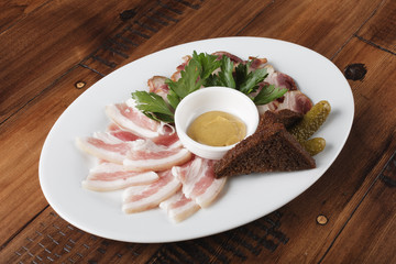 smoked and salted lard on a white oval plate. bacon with sauce and greens. cold meat appetizer. wooden background.