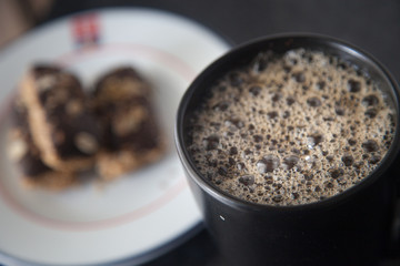 Overhead view of black cup of coffee and a plate with biscuits close up