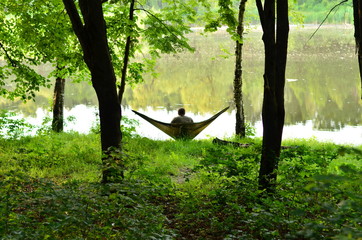 A man rests in a hammock in the woods by the river