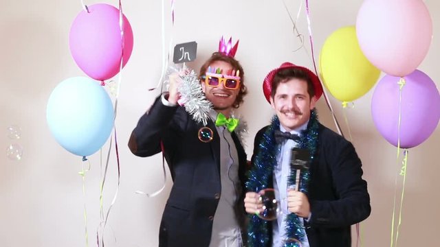 Two male friends having fun dancing with boards in love in party photo booth 