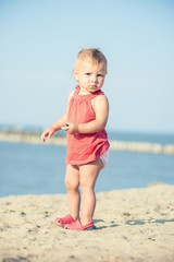 Baby playing on the sandy beach near the sea. Cute little girl in red dress with sand on tropical beach. Ocean coast.