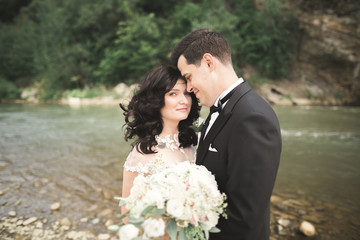 Bride and groom holding beautiful wedding bouquet. Posing near river