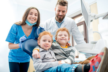 Obraz premium Portrait of happy young boys sitting on the chair with dentist and woman assistant at the dental office
