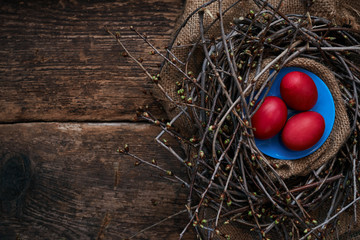 Three Easter eggs, on a blue plate in the nest with spring branches
