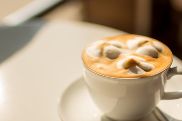 White cup of lattte coffee with sun rise lighting selective focus.
