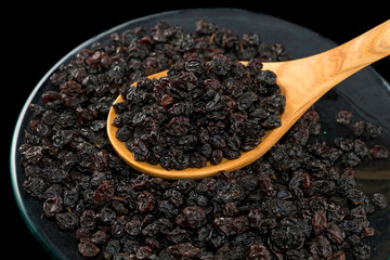 Black raisins in plate with wooden spoon