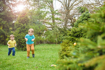 Kids on Easter egg hunt in blooming spring garden. Children searching for colorful eggs in flower meadow. Toddler boy and his brother friend kid  play outdoors