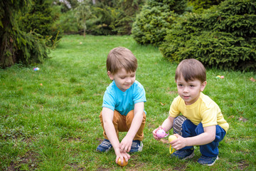 Kids on Easter egg hunt in blooming spring garden. Children searching for colorful eggs in flower meadow. Toddler boy and his brother friend kid  play outdoors