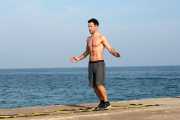 Athletischer Mann macht Training an Koordinationsleiter am Meer