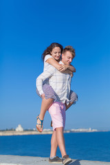 Fototapeta na wymiar Piggyback. Young man carrying girl along seafront