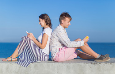 Attractive couple sitting back to back on seafront