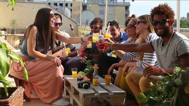 Group of happy multi-ethnic friends looking at camera and toasting with cocktails at rooftop party on beautiful sunny day
