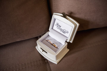 Wedding rings in box with inscription "Ring wed" on brown textile background