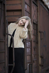 Blond young woman wear sheep jacket and black long skirt among of a wagons train