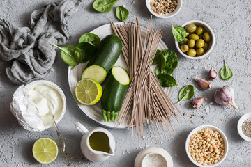 Ingredients for making green soba bowl - zucchini, spinach, soba, yogurt on grey background, top view. Healthy vegetarian food concept. Flat lay
