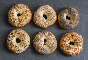 Homemade bagels with a variety of seeds on a gray background, top view. Food background