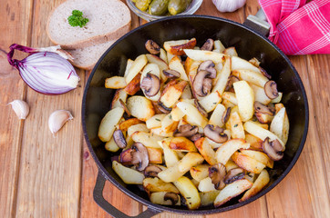 Fried potatoes with mushrooms in a pan on a wooden background