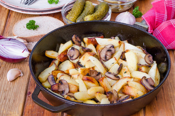 Fried potatoes with mushrooms in a pan on a wooden background
