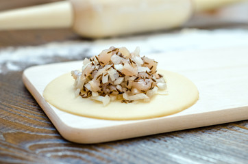 Circle of raw dough with white meat and onions, on a wooden board, rolling pin and flour