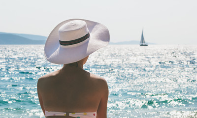 Young woman with hat sitting by the sea in summer