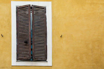 Wooden window with closed shutters and white broad frame on an old yellow painted wall of a house in the center of Rome, Italy. Vintage background with a space for text (copy space)