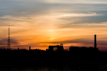 Fototapeta na wymiar Dramatic sunset over the city silhouette near water