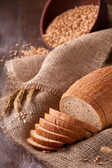 Slices of bread on burlap on the wooden table. composition with wheat ears scattered around and ears of wheat.