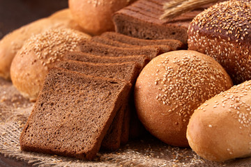 Assortement of bread on burlap on the wooden table. Slices of bread and roll.
