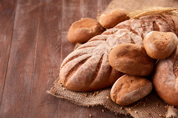 handmade tasty bread lying on burlap on the wooden table with flour, wheat and ears of wheat