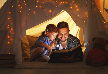 happy family father and child daughter reading a book  in  tent at home.