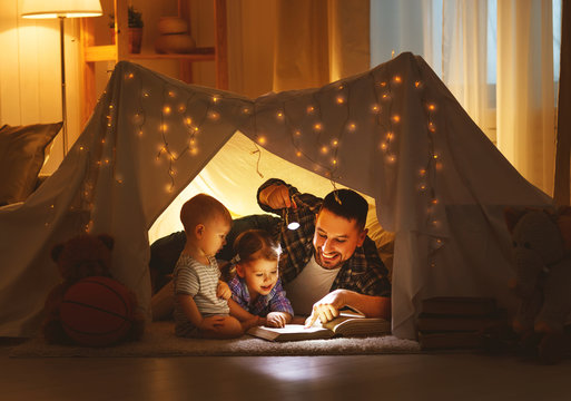 happy family father and children reading a book  in  tent at home.