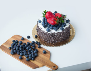 photo of delicious tasty cake with fresh strawberries and blueberries and cutting board with blueberries on the wonderful white background