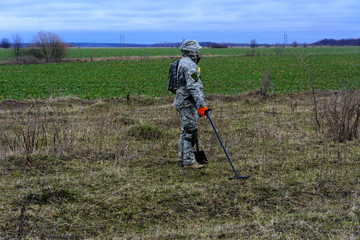 Man with a device for finding treasures with a shovel on the field