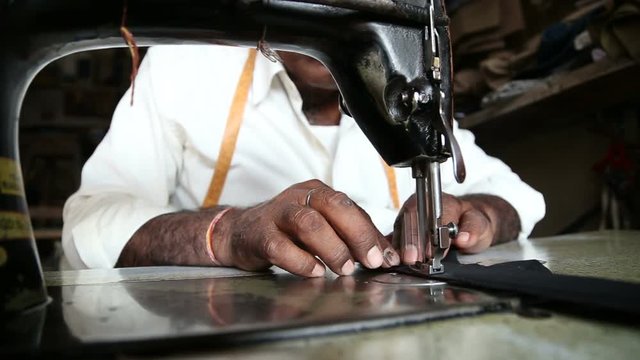 Man sewing on a sewing machine and cutting the thread with scissors, closeup.