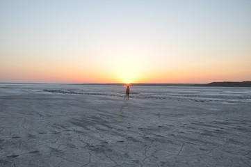 The sun is setting over the mud lake and a lonely figure at the horizon