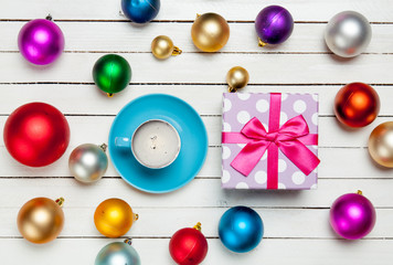photo of blue cup of coffee and cute gift near colorful baubles on the wonderful white wooden background