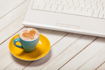 photo of beautiful blue cup of coffee and laptop on the wonderful white wooden background