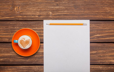 Obraz na płótnie Canvas photo of beautiful blue cup of coffee and sheet of paper with pencil on the wonderful brown wooden background