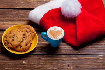 Obraz na płótnie Canvas photo of plate full of cookies, santa claus hat and cup of coffee on the wonderful brown wooden background