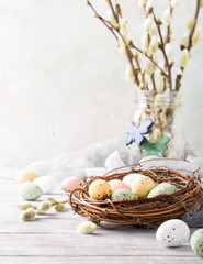 Easter composition of colorful quail eggs in the nest on the light wooden background. Holiday...