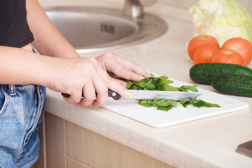 girl cuts a greens on a board on a kitchen.