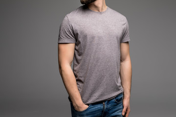 A man in a grey t-shirt and denims holds his hands in pockets.
