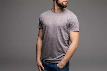 A man in a grey t-shirt and denims holds his hands in pockets.