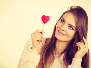 Flirty woman holding red wooden heart on stick