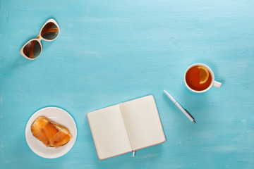 Flat lay composition of diary, glasses, pen, cup of tea and salmon sandwich on blue wooden desk
