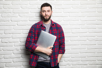 Happy young man show laptop in hands against brick wall