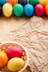 Multicolored easter eggs, and basket with eggs on a textured wooden background. The concept of a holiday and a happy Easter. A sheet of crumpled paper with space for text