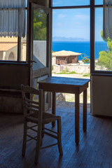 Greece romantic composition: table and chair near the window and deep blue sea behind 