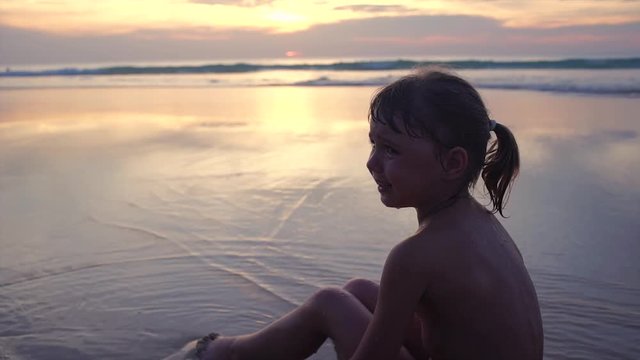 Little girl crying on the shore of the ocean at sunset
